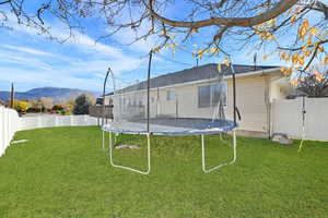 Back of property with a fenced backyard, a trampoline, a gate, and a mountain view