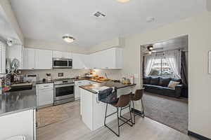Kitchen featuring appliances with stainless steel finishes, a breakfast bar area, white cabinets, a peninsula, and a textured ceiling