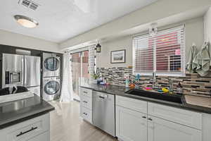 Kitchen with stainless steel appliances, dark countertops, light wood-style flooring, white cabinets, and a textured ceiling