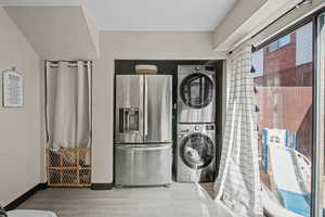 Laundry area featuring wood finished floors and stacked washing machine and dryer