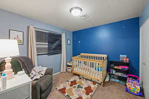 Bedroom featuring a nursery area, carpet flooring, and a textured ceiling