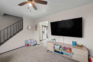 Living room with stairway, carpet, stacked washer / dryer, and a ceiling fan