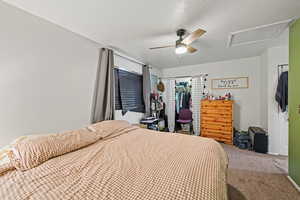 Carpeted bedroom featuring attic access, a closet, and a ceiling fan