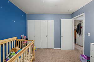 Bedroom featuring light colored carpet, a crib, and a closet