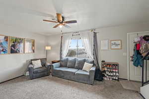 Living room with a textured ceiling, carpet floors, and ceiling fan