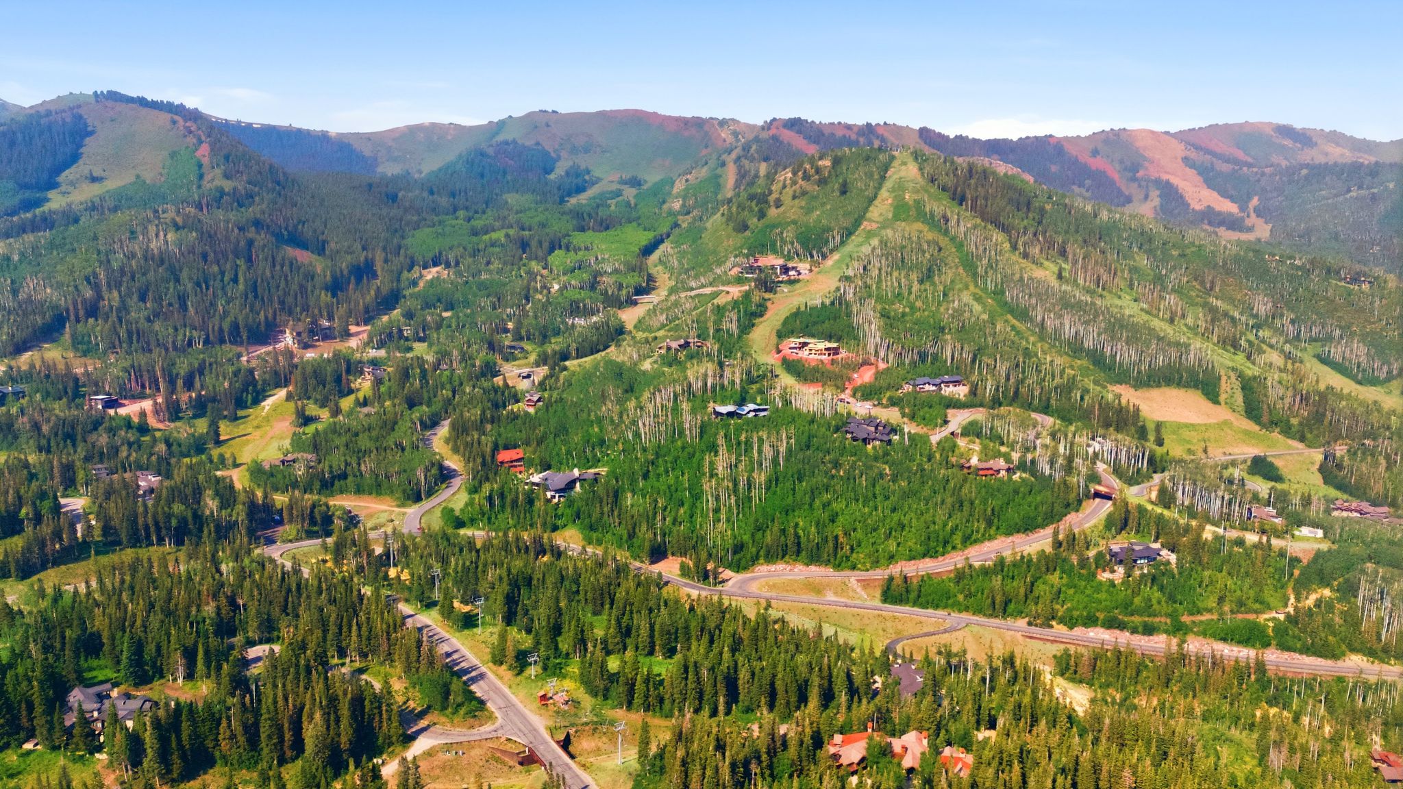Expansive mountain landscape featuring dense evergreen forests and scattered residential properties, with paved roadways traversing the terrain