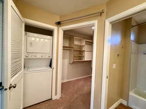 Laundry area with stacked washer / dryer, light carpet, and a textured ceiling