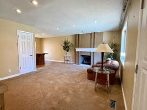 Living area conveniently located adjacent to the kitchen and dining, featuring a brick fireplace, recessed lighting, light carpet, and a textured ceiling