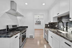Kitchen featuring appliances with stainless steel finishes, dark stone countertops, wall chimney exhaust hood, white cabinets, and recessed lighting