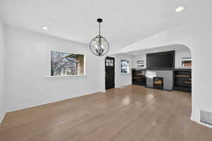 Unfurnished living room with light wood-type flooring, arched walkways, a lit fireplace, recessed lighting, and a chandelier