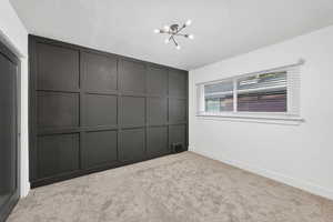 Unfurnished bedroom with a chandelier, a textured ceiling, a closet, and light carpet