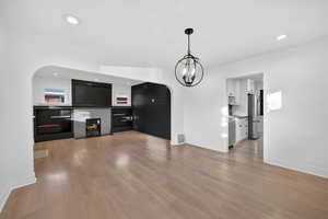 Unfurnished living room with arched walkways, light wood finished floors, a lit fireplace, and recessed lighting