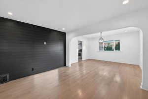 Unfurnished living room featuring arched walkways, light wood-style flooring, an accent wall, recessed lighting, and wooden walls