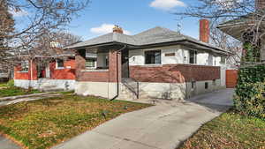 View of front of home featuring brick siding, a chimney, roof with shingles, and a front yard