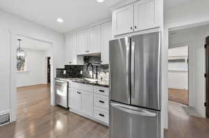 Kitchen with stainless steel appliances, arched walkways, white cabinets, light wood-type flooring, and recessed lighting