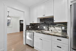 Kitchen with dark stone counters, white cabinets, appliances with stainless steel finishes, decorative backsplash, and light wood finished floors
