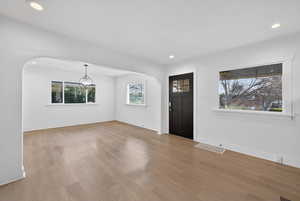 Foyer entrance with arched walkways, light wood-style floors, recessed lighting, and a chandelier