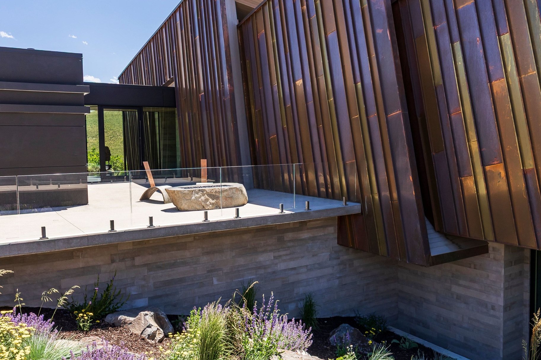 Modern architectural design featuring varied copper-toned metal siding and a stone-clad base
