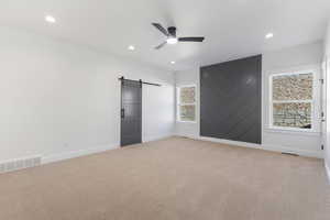 Unfurnished bedroom featuring a barn door, light colored carpet, a ceiling fan, and recessed lighting