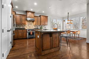Kitchen with pendant lighting, a center island with sink, stainless steel appliances, a kitchen bar, and brown cabinets