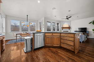 Kitchen with a center island, brown cabinets, dark wood-style floors, stainless steel dishwasher, and pendant lighting