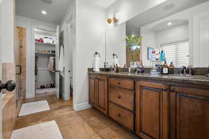 Main Suite Bathroom featuring a walk in closet, double vanity, a stall shower, stone tile floors, and recessed lighting