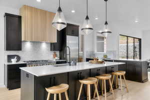 Kitchen featuring light stone counters, a kitchen breakfast bar, a large island with sink, pendant lighting, and recessed lighting