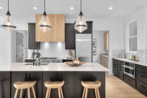 Kitchen with a breakfast bar area, light stone counters, pendant lighting, light wood-style flooring, and recessed lighting