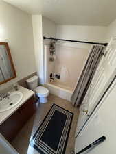 Full bath featuring vanity, shower / bathtub combination with curtain, a textured ceiling, and light tile patterned floors