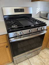 Kitchen view of brown cabinetry, light countertops, and stainless steel range with gas stovetop