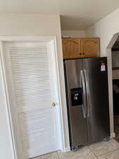 Kitchen featuring stainless steel fridge with ice dispenser, brown cabinetry, a textured ceiling, arched walkways, and light tile patterned floors