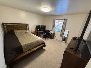 Bedroom with light colored carpet, a textured ceiling, and a desk