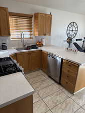 Kitchen with light countertops, dishwasher, gas range oven, a peninsula, and brown cabinets