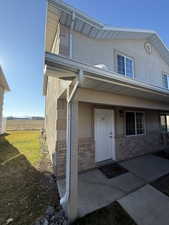 Doorway to property featuring stucco siding, a porch, brick siding, and a rural view