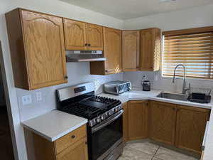 Kitchen featuring gas stove, light countertops, brown cabinets, and under cabinet range hood