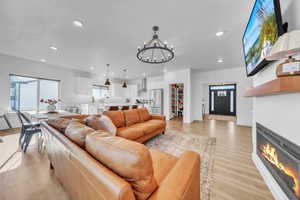 Living area featuring light wood-style flooring, recessed lighting, a chandelier, and a glass covered fireplace