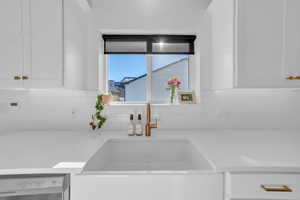 Kitchen view of white cabinetry, dishwasher, light stone counters, and decorative backsplash