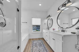 Full bath with double vanity, a shower stall, light wood-style flooring, and a bath
