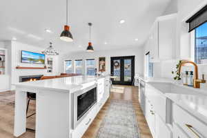 Kitchen featuring white cabinetry, a kitchen island, a warm lit fireplace, a breakfast bar area, and recessed lighting