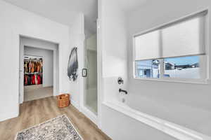 Full bathroom featuring a shower stall, a spacious closet, a garden tub, and light wood-type flooring