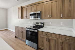 Kitchen featuring stainless steel appliances, light wood-style flooring, and brown cabinetry