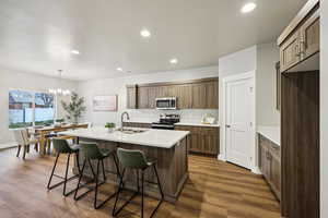 Kitchen with a kitchen island with sink, a kitchen bar, stainless steel appliances, a chandelier, and dark wood-style flooring