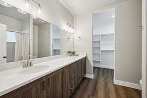 Bathroom with double vanity, a shower with shower curtain, dark wood-style floors, and a walk in closet