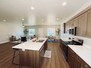 Kitchen with stainless steel appliances, a breakfast bar, dark wood-style flooring, open floor plan, and a center island with sink