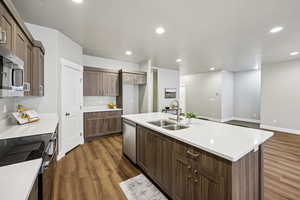 Kitchen with dark wood finished floors, a center island with sink, stainless steel appliances, recessed lighting, and light stone countertops