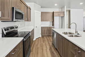 Kitchen with appliances with stainless steel finishes, dark wood-type flooring, light stone countertops, recessed lighting, and brown cabinets