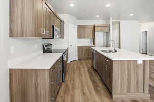 Kitchen featuring appliances with stainless steel finishes, an island with sink, light wood-style floors, recessed lighting, and brown cabinets