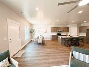 Kitchen with a kitchen bar, light countertops, a ceiling fan, a kitchen island with sink, and light wood finished floors