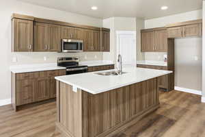 Kitchen with stainless steel appliances, a kitchen island with sink, light wood finished floors, light stone counters, and recessed lighting