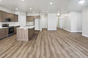 Kitchen with appliances with stainless steel finishes, recessed lighting, a kitchen island with sink, light wood-style flooring, and open floor plan